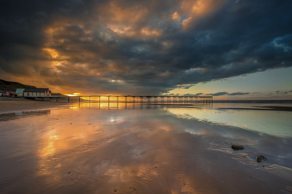 Sunset over Saltburn Pier, the wet sand reflecting the sky.